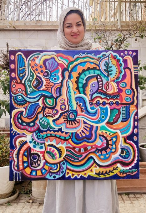 A woman wearing a beige hijab and dress proudly displays a vibrant, colorful abstract painting featuring psychedelic patterns and bold neon hues.