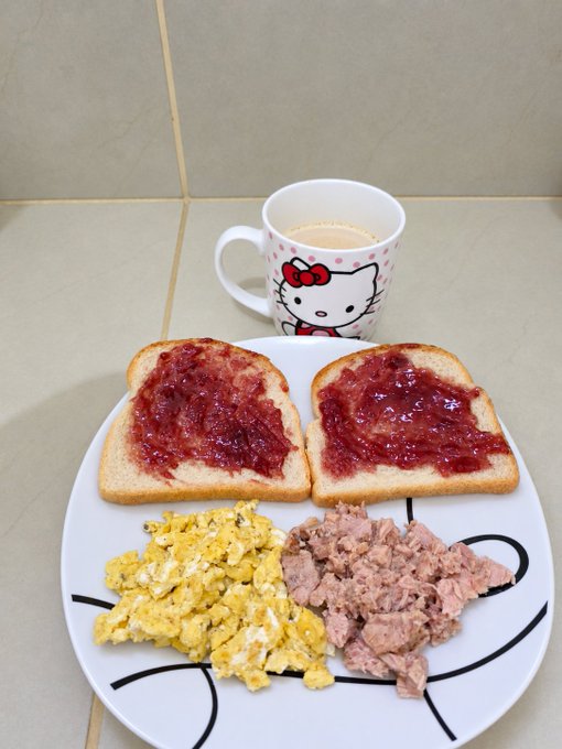A breakfast plate on a tiled surface with jam toast, scrambled eggs, tuna, and a Hello Kitty mug of coffee.