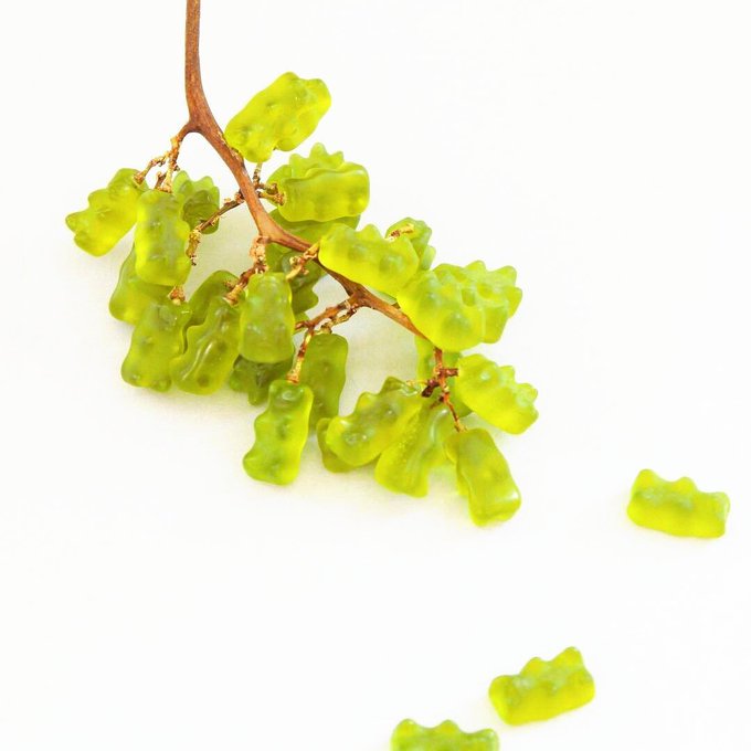 A cluster of translucent green bear-shaped gummy candies arranged on a stem branch against a white background.