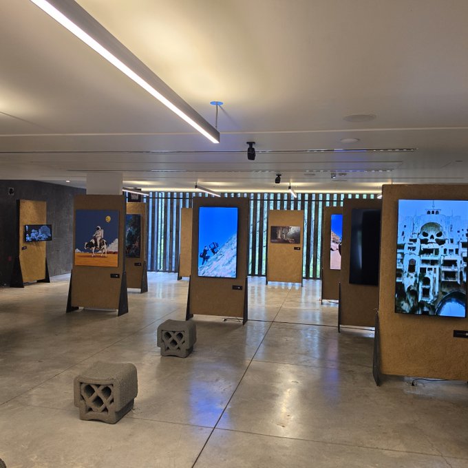 An art gallery exhibition displaying various photographs on wooden panels, with decorative concrete blocks placed on the polished floor.
