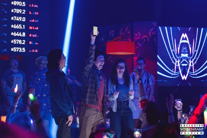 A man holds up a glowing phone at what appears to be a crypto-themed party, with a scoreboard displaying values like "+$890.5" and "+$789.2" visible behind him, alongside digital eye graphics — a scene from "The Altruists," a limited series inspired by the FTX collapse and Sam Bankman-Fried's downfall.