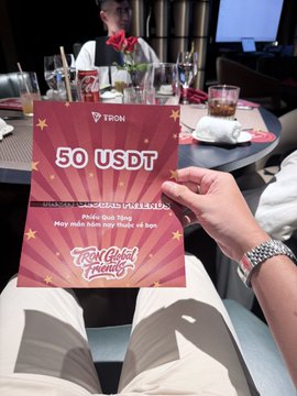 A guest holds a red TRON giveaway card reading “50 USDT” at a dinner table. The scene reflects the warm, memorable gathering shared with @trondao, @TronDao_VIE, and fellow community members, tagged #TRONGlobalFriends.