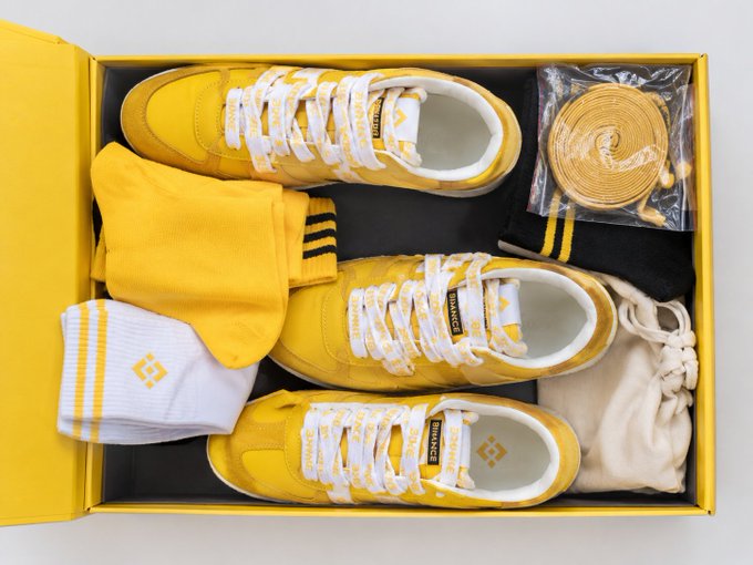 A yellow shoe box displaying a pair of yellow sneakers with white laces, accompanied by yellow socks, a white sweatband with a diamond logo, and extra shoelaces.