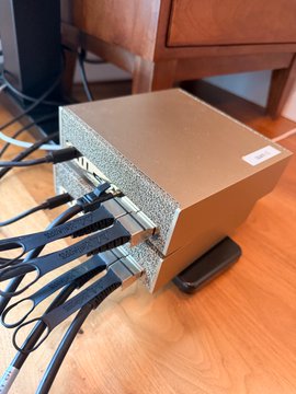 A metallic network switch or router with multiple ethernet cables connected to its ports, sitting on a wooden floor.
