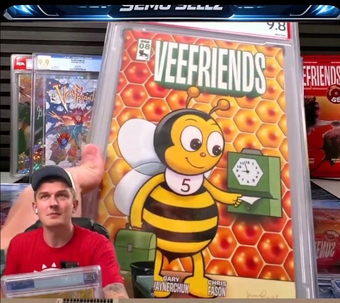 Man in a red shirt holding up a CGC-graded 9.8 Veefriends #08 comic book cover featuring a cartoon bee character.