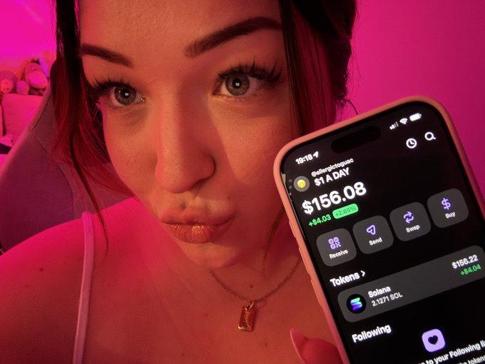 The image features a young woman with brown hair dressed in white, holding up a cell phone displaying an app for Bitcoin trading. The text at the bottom of the picture reads "day 208 of buying $1 worth of SOL until ATH". It seems like she might be reviewing her Bitcoin investments or checking out a new trend related to Bitcoins.