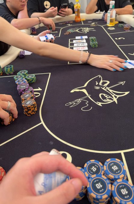 A first-person view of a Texas Hold'em poker game at a table featuring a shark logo, with stacks of chips marked "5," "10," and "100" visible along with "J1" and "J2" position markings. The scene captures the player's hand holding a winning hand while surrounded by chips and fellow players, tying into the caption's narrative about newfound gambling luck after paying respects to the God of Wealth.