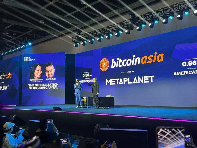 Bitcoin Asia conference stage presented by Metaplanet, featuring Ronnie Chuang and Justin Sun discussing 'The Globalization of Bitcoin Capital' with Bitcoin and American Bitcoin sponsorship banners visible.