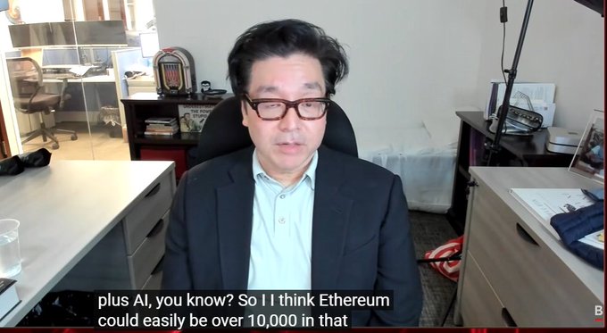 A man with glasses in a dark blazer and light blue shirt speaks in an office setting, with on-screen subtitles reading 'plus AI, you know? So I I think Ethereum could easily be over 10,000 in that'.