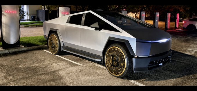 A silver Tesla Cybertruck parked at a Tesla Supercharger station at night, featuring custom gold Bitcoin emblem wheels.