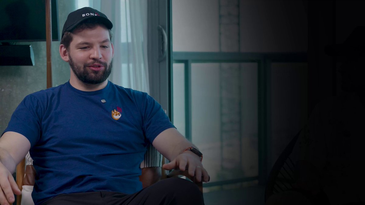 The image features a man sitting in a chair, wearing a blue shirt with a black baseball cap. The background shows a window that allows natural light into the room. There are also two other people visible in the scene, one of whom appears to be a woman and the other a man. The image is related to the post because it contains text discussing the failure rate of startups and how crypto companies can survive.