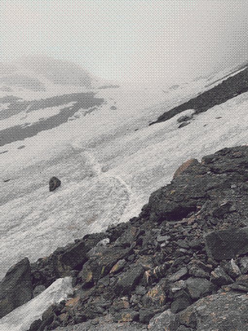 A desolate, snowy landscape features rocky terrain in the foreground with a faint peace sign traced into the snow.