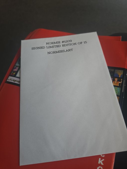 A white sheet of paper with typed text reading "NORMIE #1209, SIGNED LIMITED EDITION OF 15, NORMIES.ART" rests on a red folder, showcasing a rare and vaulted collectible from @normiesART that the poster saved from being locked away, as referenced in their post about securing this sealed edition of 15 with help from @serc1n.
