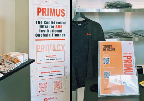 A display booth for Primus featuring promotional banners describing it as 'The Confidential Infra for BNB Institutional Onchain Finance' with privacy and confidentiality features, alongside a black Primus sweatshirt and informational materials.