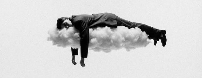 Black and white surreal image of a man in a suit lying horizontally on a small cloud, with one arm dangling downward.