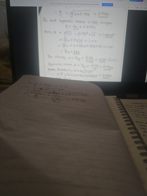 A handwritten notebook filled with physics equations about hydraulics sits in front of a computer screen displaying similar calculations on lined paper.
