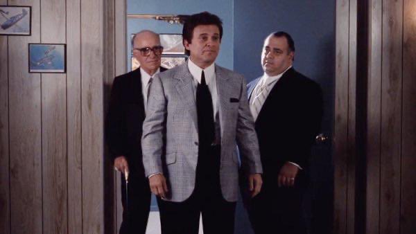 Three men in suits stand in a wood-paneled room, with a bespectacled bald man on the left, a mustachioed man in a light gray suit in the center, and a heavier-set man in a dark suit on the right. The scene evokes classic mob film imagery, humorously suggesting Leopold as a comically overconfident buyer making a risky "AI trade" bet right as the market signals caution—much like a mob boss walking into an ambush he doesn't see coming.