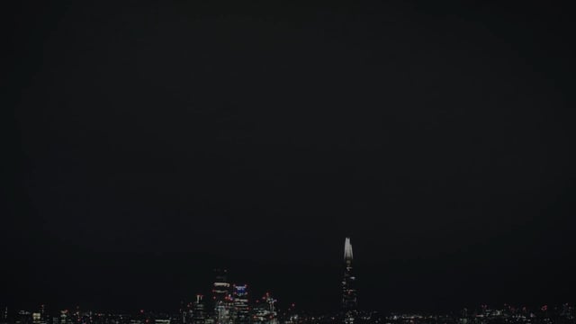 A nighttime cityscape photograph showing a dark skyline with illuminated skyscrapers, prominently featuring the Salesforce Tower lit up in white in the center.