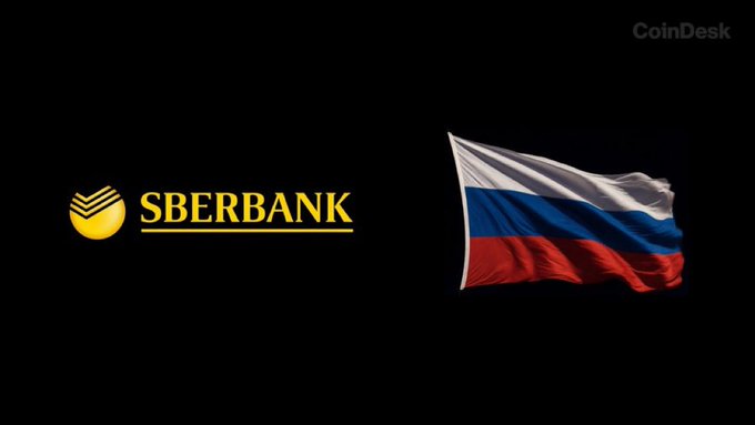 The image shows the Sberbank logo (in yellow) alongside a waving Russian flag (white, blue, and red) on a black background, with "CoinDesk" branding in the top right corner. This visual accompanies news about Russia's largest bank, Sberbank, planning to develop cryptocurrency trading infrastructure by December 1, following recent legislation passed by the State Duma on July 21.
