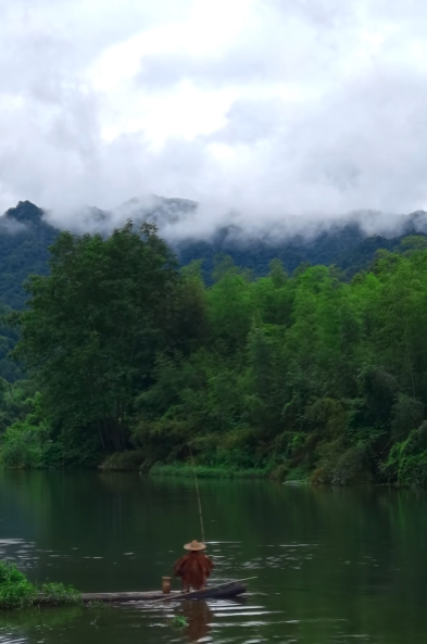 A serene scene of a person in a wide-brimmed hat rowing a small wooden boat on a calm, misty river, surrounded by lush green trees and mountains shrouded in low-hanging clouds.