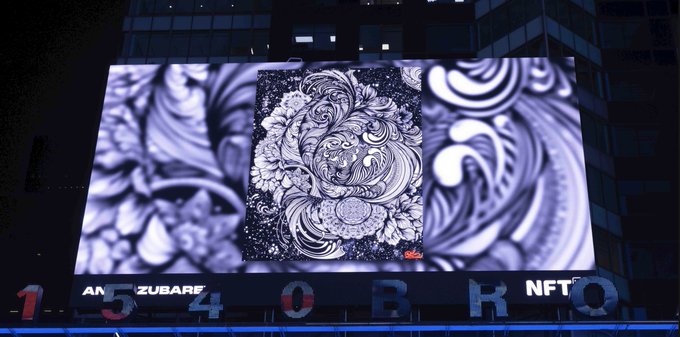 A large illuminated outdoor digital billboard at night displays an intricate black-and-white ornamental artwork featuring a lion's head, with the text 'AMAZUBARF', '154', 'OBRO', and 'NFTQ' visible along the bottom edge.