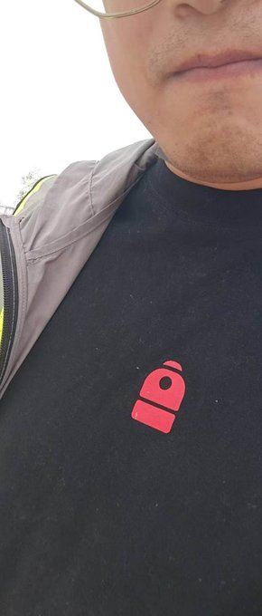A person wearing a black T-shirt featuring the pink "B" logo of Backpack, a crypto project, poses for a close-up selfie. The image highlights the brand's apparel, tying into the post's mention of the Backpack platform and its new AI search feature.