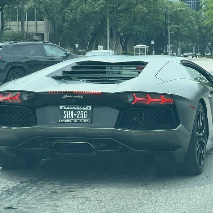 A grey Lamborghini Aventador is shown from the rear, featuring a Texas license plate that reads "SHA-256," directly matching the text mentioned in the accompanying post.