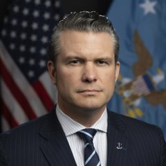 An official portrait of a man in a dark suit and striped tie standing in front of American and military flags.