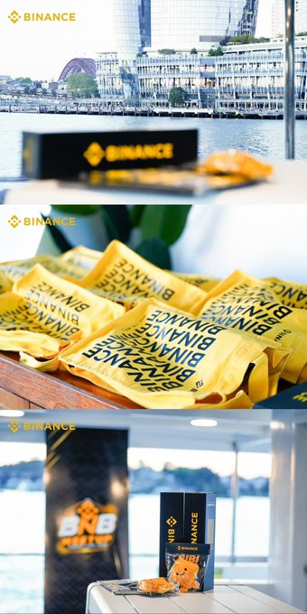 A promotional collage for Binance featuring branded merchandise including yellow 'BINANCE CUP' snack packages and 'VIB' branded items, set against a waterfront city backdrop.