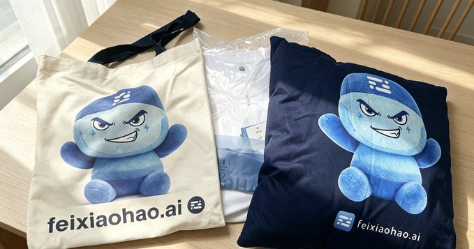 A cream-colored tote bag and dark blue pillow featuring a blue cartoon mascot character, both branded with 'feixiaohao.ai' logo, sitting on a light wooden table in sunlight.