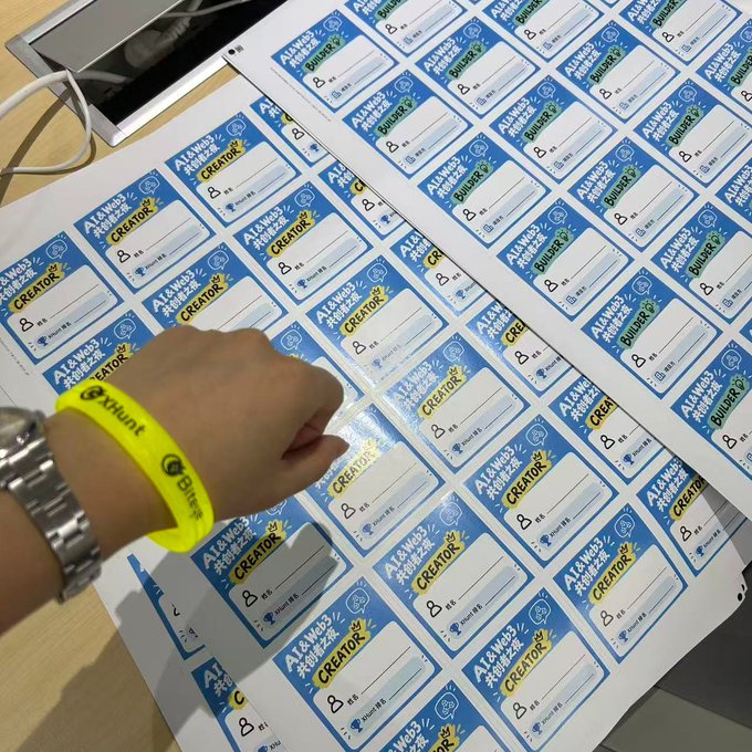 A person wearing a yellow 'BitAnt' wristband signs sheets of 'AI & Web3' CREATOR and BUILDER name badges.