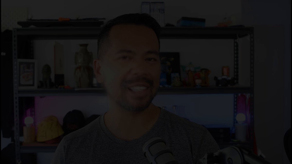 The image shows a man wearing a gray shirt holding a microphone, smiling at the camera while standing in front of a bookshelf filled with various items such as vases and figurines. The background appears to be a room or office setting, which could potentially be related to the content of the post about a police forensics workflow on Cardano.