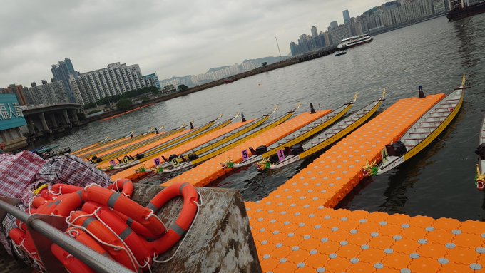 Dragon boats lined up at a Hong Kong harbor venue, with orange pontoons stretching along the water and life preservers stacked in the foreground, confirming the post's note that the dragon boat location hadn't changed despite the 32°C heat on 6/26.