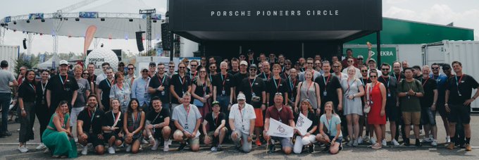A large group of people poses for a photo in front of a stage labeled 'PORSCHE PIONEERS CIRCLE'.
