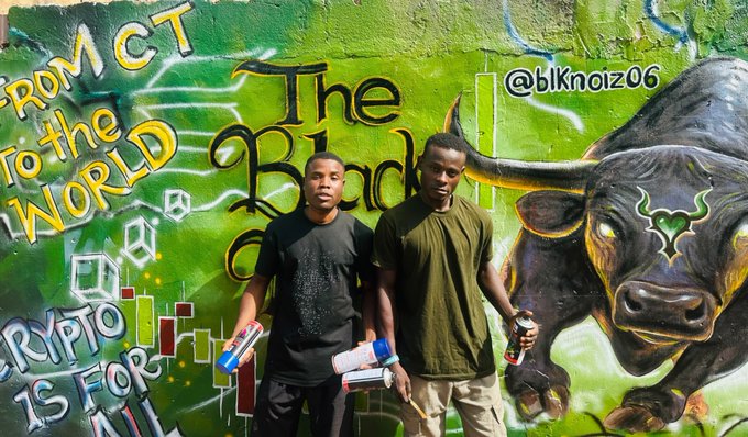 Two young men pose in front of a vibrant mural featuring a bull and the text "FROM CT TO THE WORLD," "The Black Bull," "CRYPTO IS FOR ALL," and the handle "@blknoiz06," holding spray paint cans that connect to the post's celebration of the artist and the "ANSEM" community's IRL art bounty.