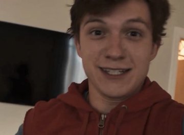 A close-up photograph shows a young man with dark hair smiling broadly while wearing a red hooded vest.