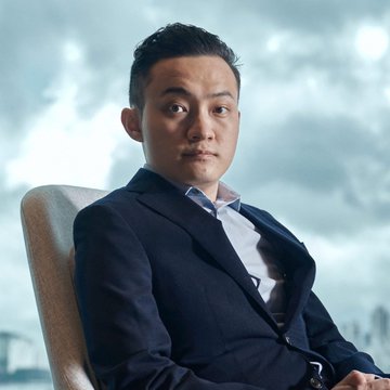 The image shows Justin Sun, the founder of TRON, seated in a dark suit and white shirt against a cloudy cityscape backdrop, visually accompanying the news of his accusations against World Liberty Financial's USD1 stablecoin.