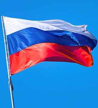 The national flag of Russia waving against a clear blue sky, featuring horizontal white, blue, and red stripes.