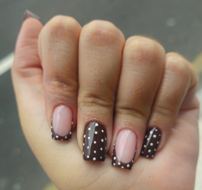 A close-up of a hand showing stylish nail art with pink, brown, and black designs featuring white polka dots.