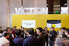 A crowd of people gathers in front of a yellow display wall with the word 'VICTION' in large white letters at what appears to be an event or convention.