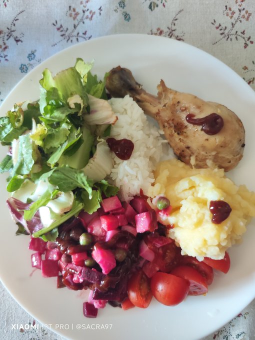 A white plate filled with a meal of chicken drumstick, white rice, mashed potatoes, green salad, beetroot salad with capers, and cherry tomatoes, photographed with a Xiaomi 13T Pro.