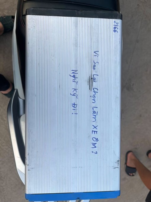 A silver car trunk with handwritten Vietnamese text reading 'VT Sao Lại Chọn Làm Xe ĐM 2' and 'Nhịn Ký Đi,' along with the number '2166.'