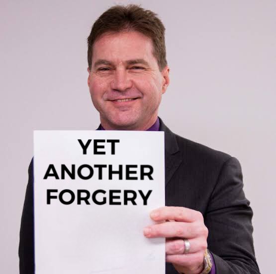 A photograph of a smiling man in a dark suit holding up a white sign with black text that reads 'YET ANOTHER FORGERY'.