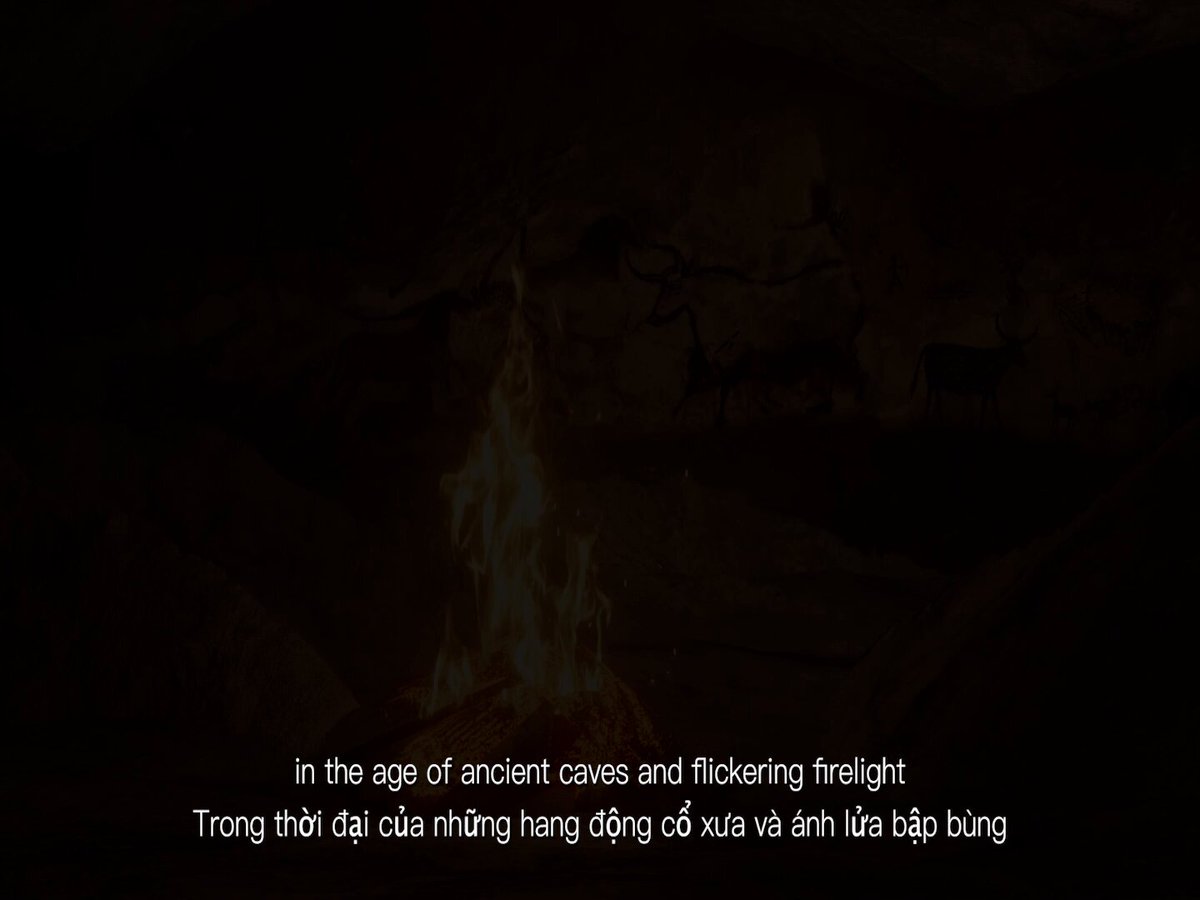 The image features a fire burning brightly, with text written above and below it that translates to "In the age of ancient caves and flickerering firelight". The fire appears to be located at the bottom right corner of the image.