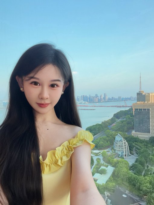 The image features a woman with long black hair wearing a yellow dress, standing next to a window overlooking a cityscape. She has her arms crossed over her chest and is posing for a photo. The caption of the image reads "GN Today I wore a Binance yellow shirt and met a new friend". This suggests that she might have been discussing or sharing information about Bitcoin with someone else while taking this picture, possibly indicating an interest in cryptocurrency or a recent transaction involving it.