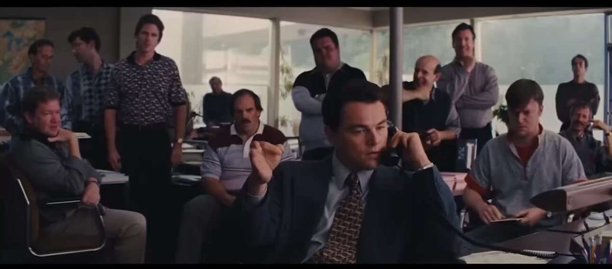The image shows a group of men sitting around a table, with one man talking on his phone while others look on. There are at least 13 people visible in the scene, some standing and others seated. The room appears to be an office setting or a meeting space, as there is a chair present near the center of the image.

The post seems to be discussing Wall Street's role in building infrastructure that kept most of the world out for over 100 years. It highlights how the gap between those two timelines has been bridged by a company called ONDO, which is working on-chain to build and maintain the necessary infrastructure within 24 months. The image captures this moment where the group of men are gathered around the table, possibly discussing or planning their next steps in this endeavor.