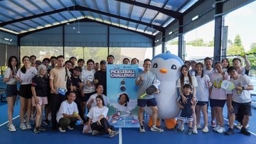 A large group of people poses for a photo at a volleyball challenge event, standing alongside a penguin mascot holding a trophy.