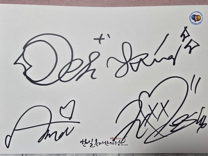A piece of paper featuring handwritten signatures in black ink, with Korean text '찾길로 찾아가는 아이돌' visible at the bottom.