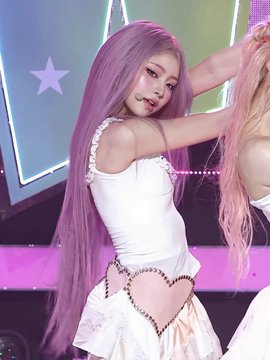 A female performer with long lavender hair wearing a white beaded top and pastel skirt, posing on a stage with star-shaped lights in the background, appearing to be a K-pop idol mid-performance.