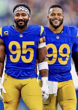 Two Los Angeles Rams players in blue and yellow uniforms with the numbers 95 and 99 smile on the field, representing the Rams team mentioned in the post about quarterbacks facing them and the Texans this season.